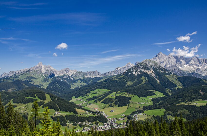 Weites Tal mit Dorf, grünen Wiesen und Wäldern vor schroffen Alpen unter klarem blauem Himmel im Sommer | © Bergbahnen Filzmoos GmbH