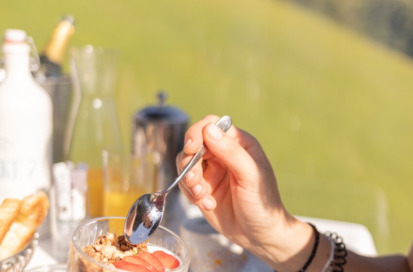 Person eating yoghurt with strawberries and granola at table inside mountain gondola in sunlight | © Großarler Bergbahnen GmbH & Co KG