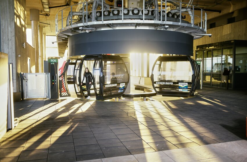 Kieserlbahn gondola station with sunlight and a passenger entering, featuring modern architecture and sharp light rays. | © Grossarler Bergbahnen GmbH & Co KG