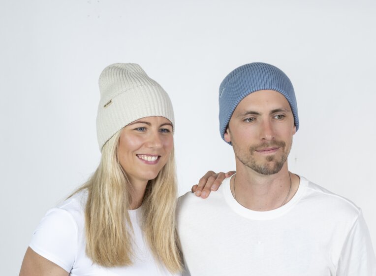 Mann und Frau mit Ski amadé Mützen posieren seitlich, Studio mit hellem Hintergrund | © Ski amadé GmbH