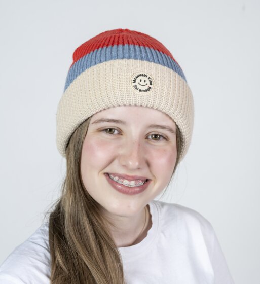 Smiling girl wearing red-beige Mountain Vibe Ski amadé beanie and white shirt | © Ski amadé GmbH