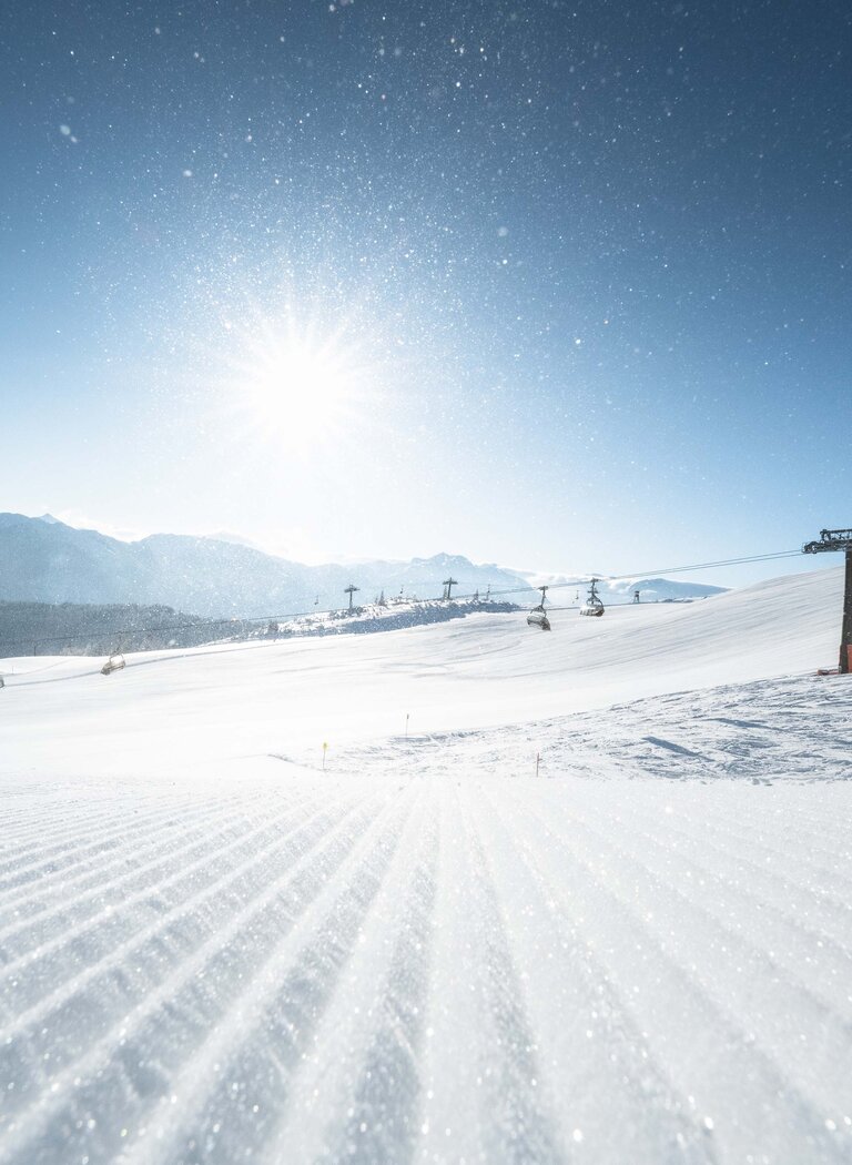 Chairlifts over a wide snowy landscape, glittering slope in front, sun rising over distant mountain ridges. | © Ski amadé GmbH