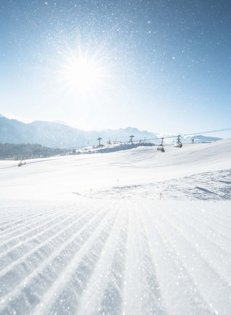 Chairlifts over a wide snowy landscape, glittering slope in front, sun rising over distant mountain ridges. | © Ski amadé GmbH
