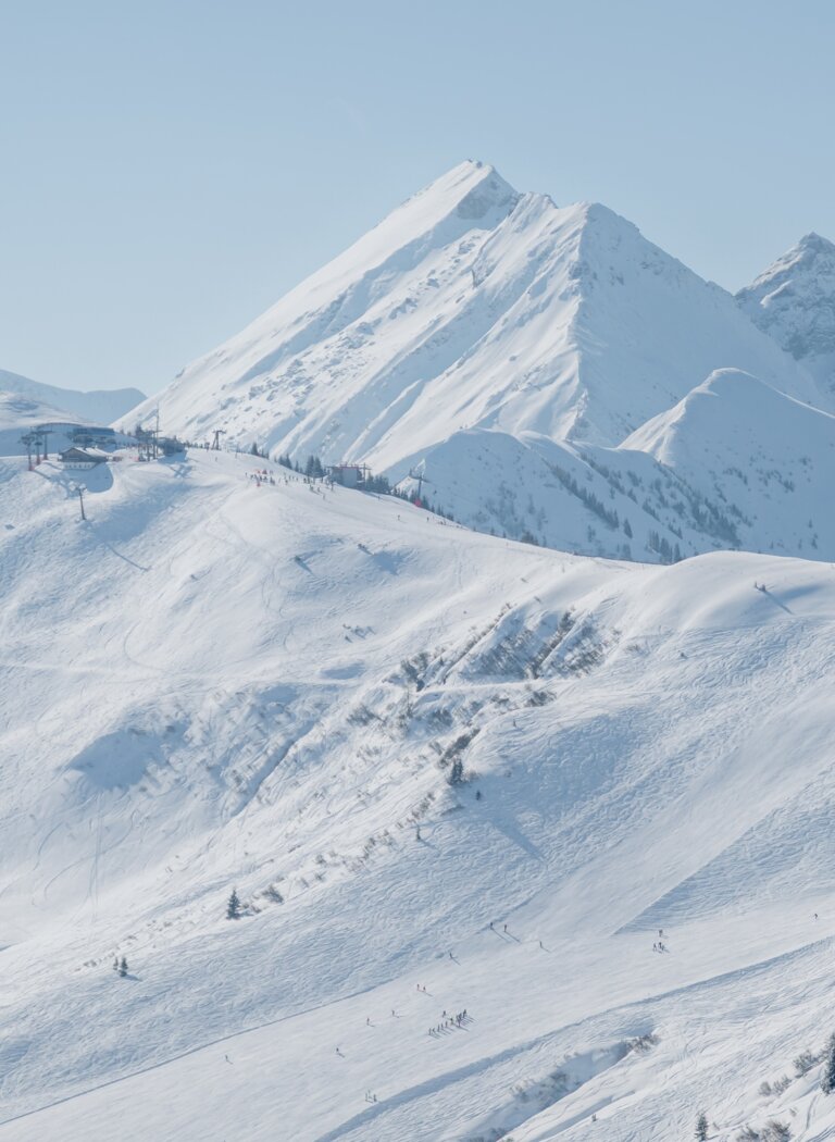 Skigebiet in den Alpen bei sonnigem Winterwetter | © Ski amadé GmbH Verschneite Alpenlandschaft mit Skipisten, Bäumen und Berggipfeln bei Sonnenschein | © Ski amadé GmbH
