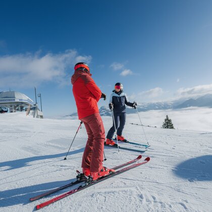 Two skiers stand on groomed slope near a mountain station, fog covering the valley with Alpine panorama | © Ski amadé GmbH