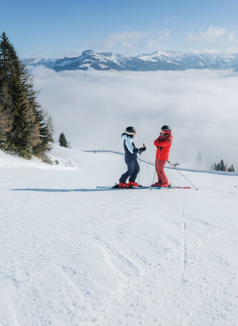 Two skiers stand on wide slope above dense sea of clouds, mountains rising under clear blue sky | © Ski amadé GmbH
