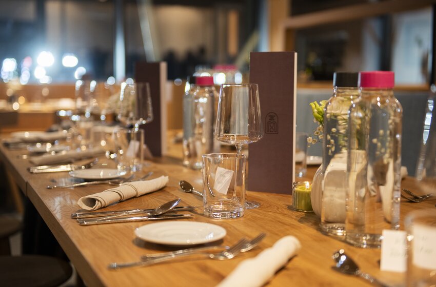 Wooden dining table set with wine glasses, cutlery, napkins, plates and several water carafes in a restaurant | © Gasteiner Bergbahnen AG 