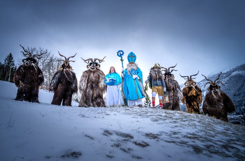 Krampus group with Saint Nicholas and companions in costumes stands on a snowy slope before forested mountains | © Gasteiner Bergbahnen AG 