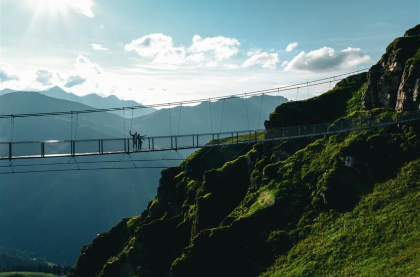 Menschen stehen auf Hängebrücke über steiler Felswand, im Hintergrund Berglandschaft und Himmel mit Wolken | © Gasteiner Bergbahnen AG