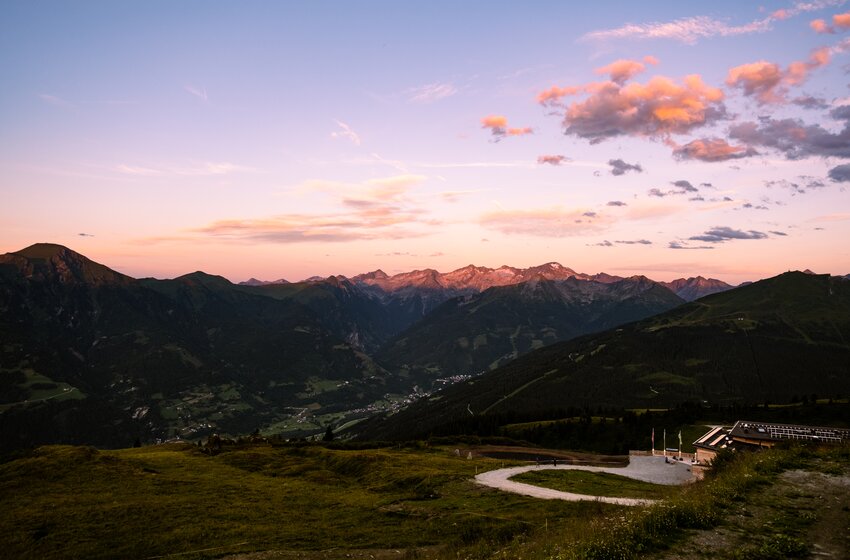 Mountain landscape with valley, peaks and lodge at dusk beneath pink clouds and a wide sky | © Gasteiner Bergbahnen AG